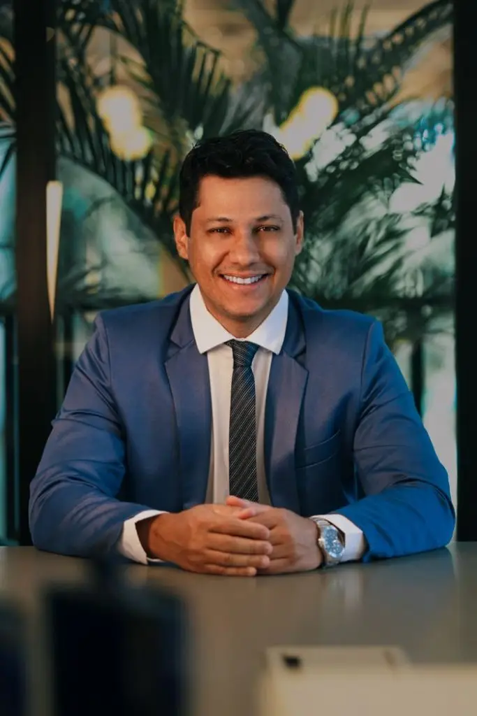 Demo Post 3 Confident businessman in a blue suit smiling at a desk in a modern office.